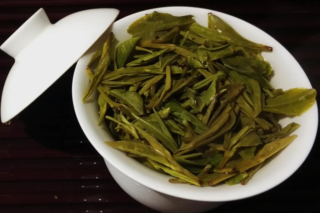 A white bowl filled with vibrant green tea leaves, accompanied by a matching lid. The mood is fresh and inviting, suggesting relaxation.