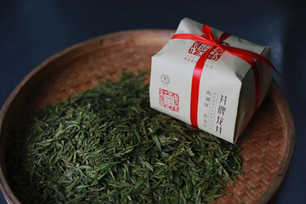 A bamboo tray filled with loose green tea leaves sits next to a neatly wrapped package tied with a red ribbon, conveying an artisanal and traditional vibe.
