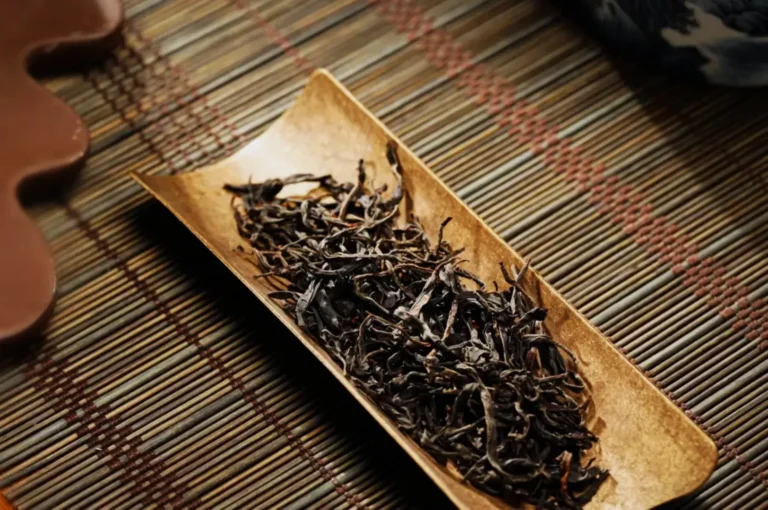 A small wooden dish containing dried tea leaves, resting on a woven mat.
