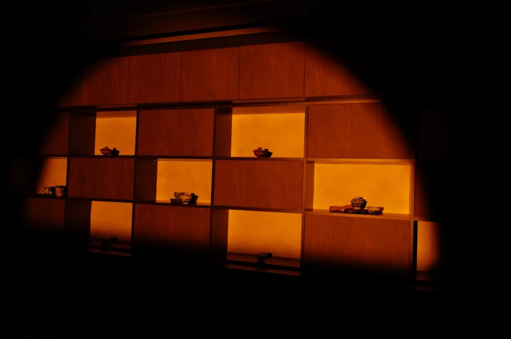 A dimly lit display with shelves illuminated in warm orange tones, holding ceramic chinese tea cups.