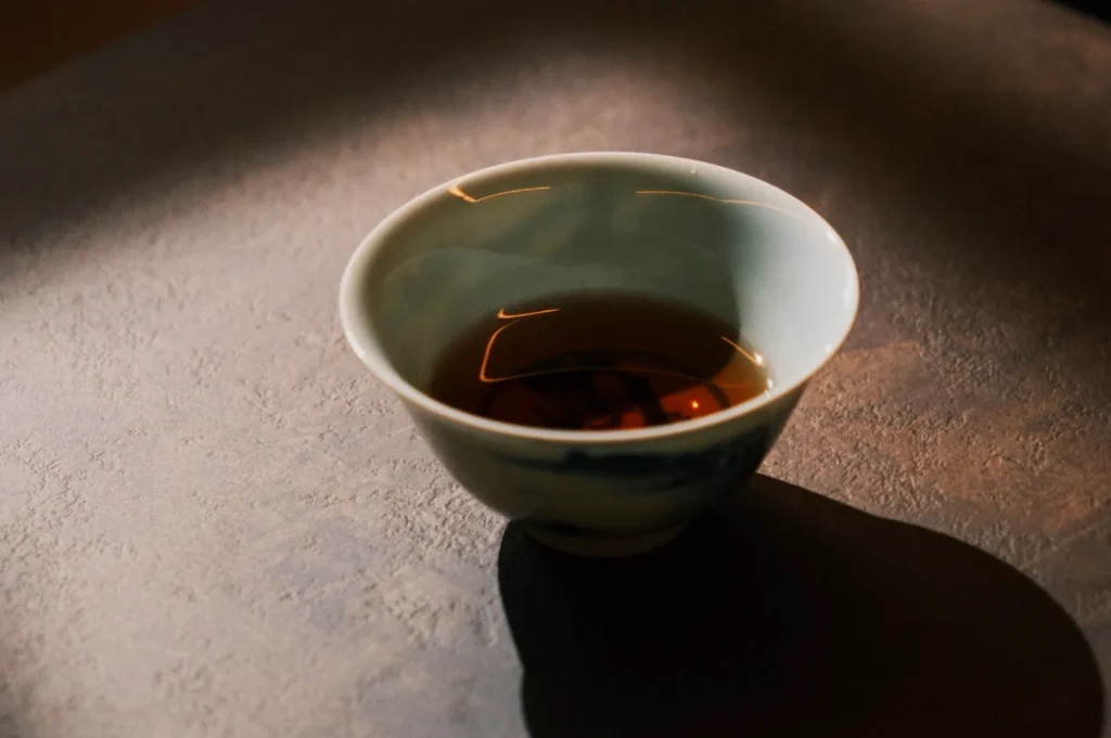 A ceramic cup of tea sits on a textured surface, illuminated by warm, soft lighting. The scene conveys a calm and inviting atmosphere.