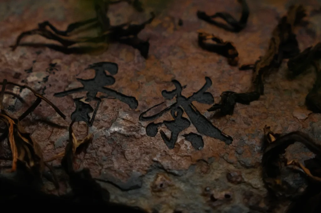 Chinese characters carved into a rusted surface with dried tea leaves surrounding them.