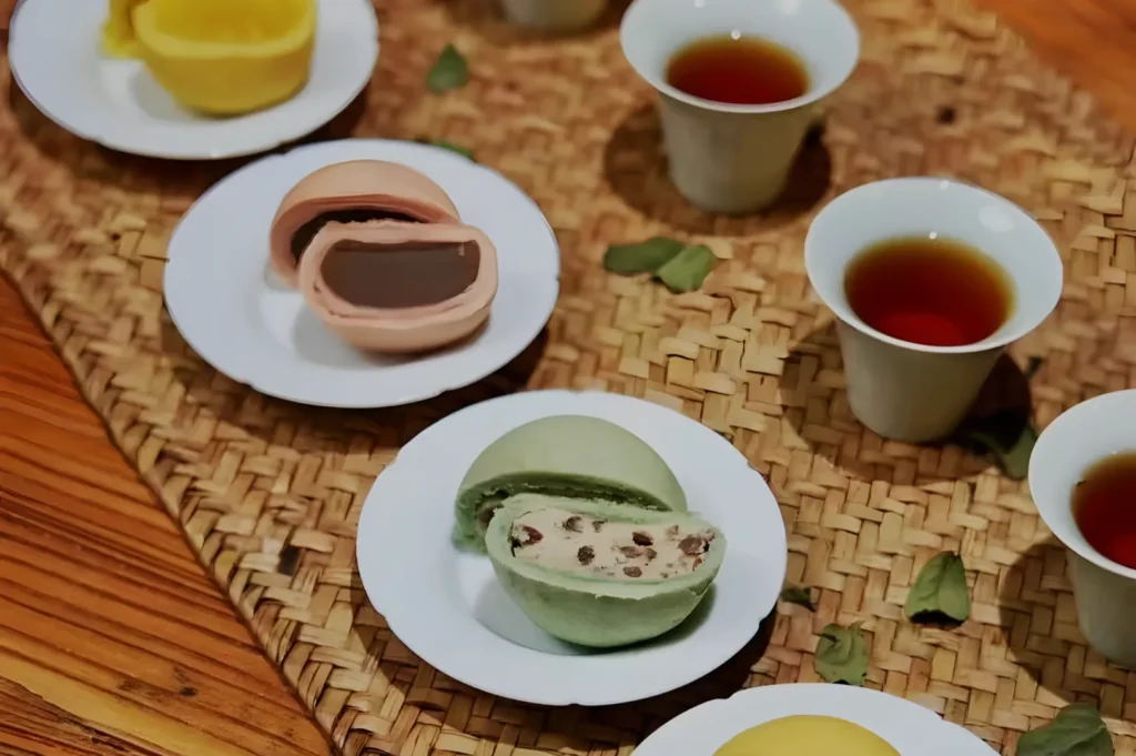 Plates of colorful mochi with various fillings are showcased alongside cups of tea on a woven mat. The scene conveys a sense of warmth and tradition.