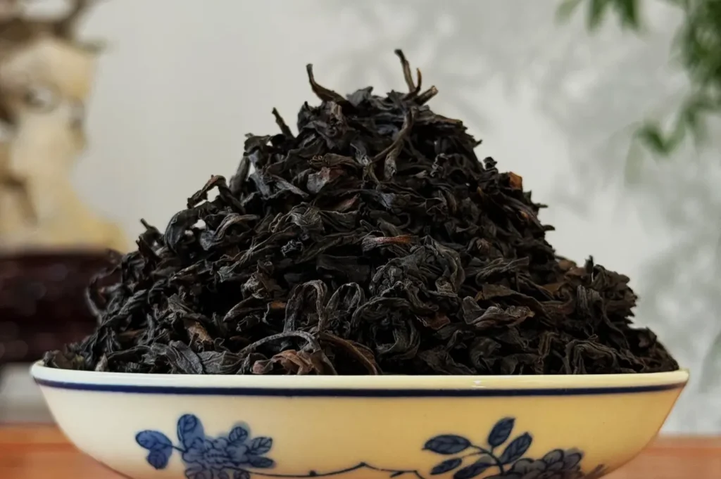 A close-up of a large pile of dried black tea leaves in a decorative bowl.