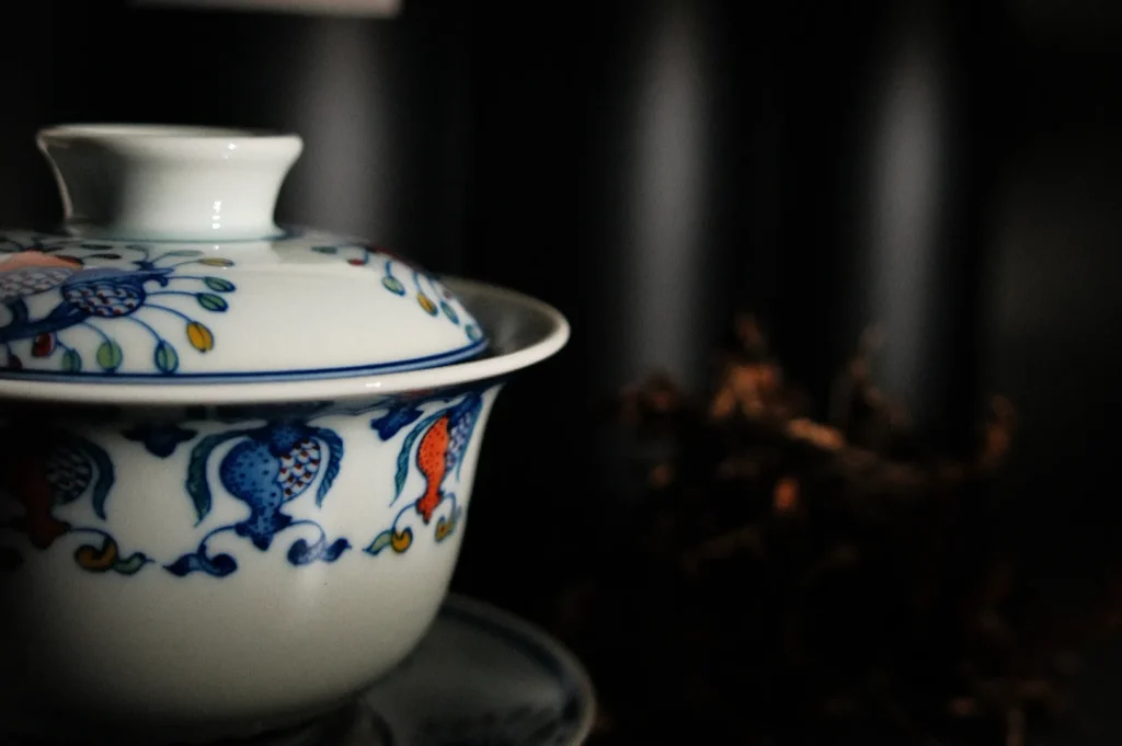 A decorative porcelain tea cup with a lid, featuring colorful floral designs, set against a dark background.