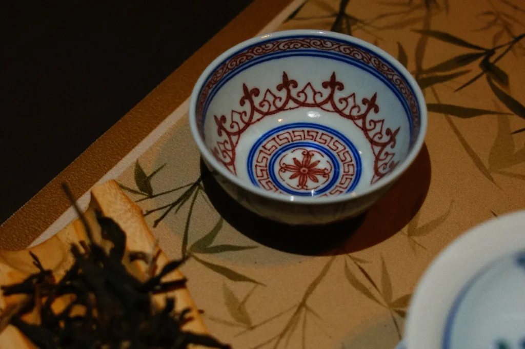 A small, decorative bowl with intricate blue and red patterns on a beige surface with bamboo designs.