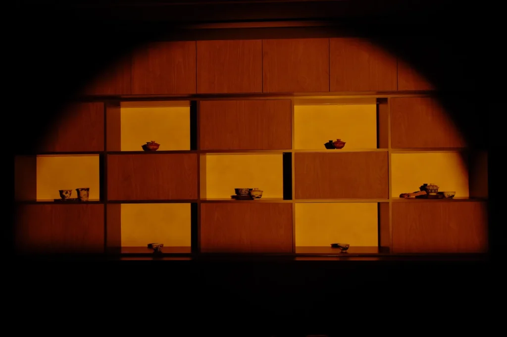 A modern shelving unit illuminated with a warm orange light, displaying various bowls and decorative items.