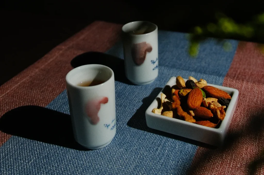 Two cups and a small dish of mixed nuts on a textured tablecloth.