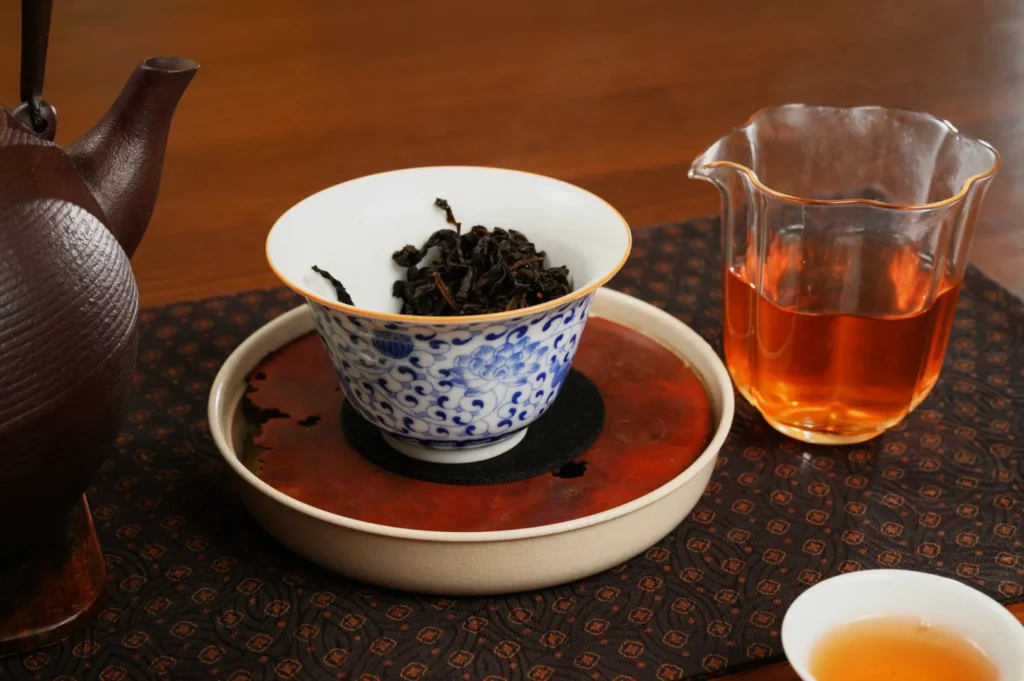 A teapot, a bowl with loose tea leaves, a glass jug of brewed tea, and a small cup on a patterned tablecloth.