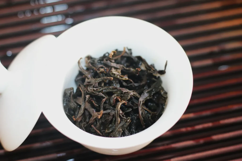 A white cup containing dried black tea leaves, placed on a wooden surface.