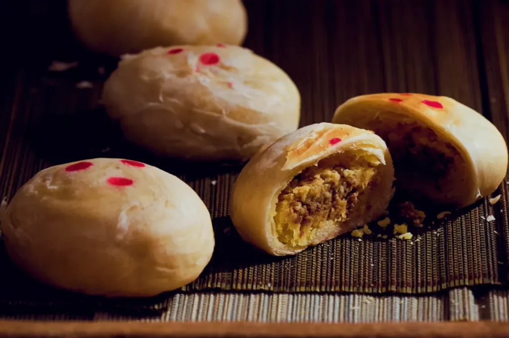 A close-up of mung bean cake filled with a yellow mixture, showing one cut open, with small red decorations on top.