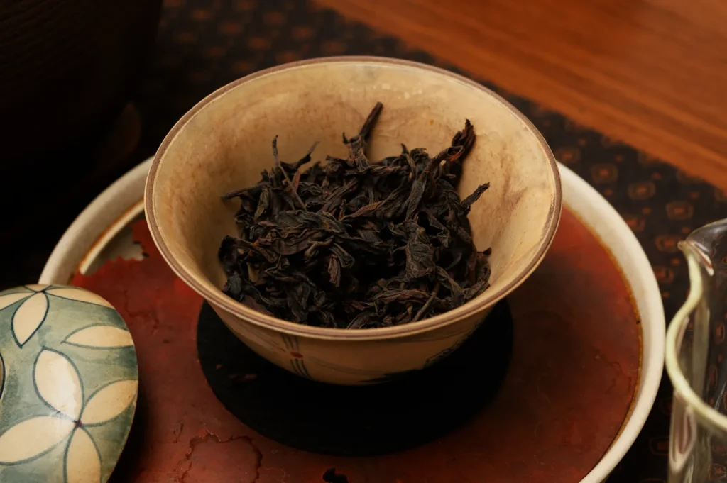 A bowl filled with dried black tea leaves, placed on a wooden surface.