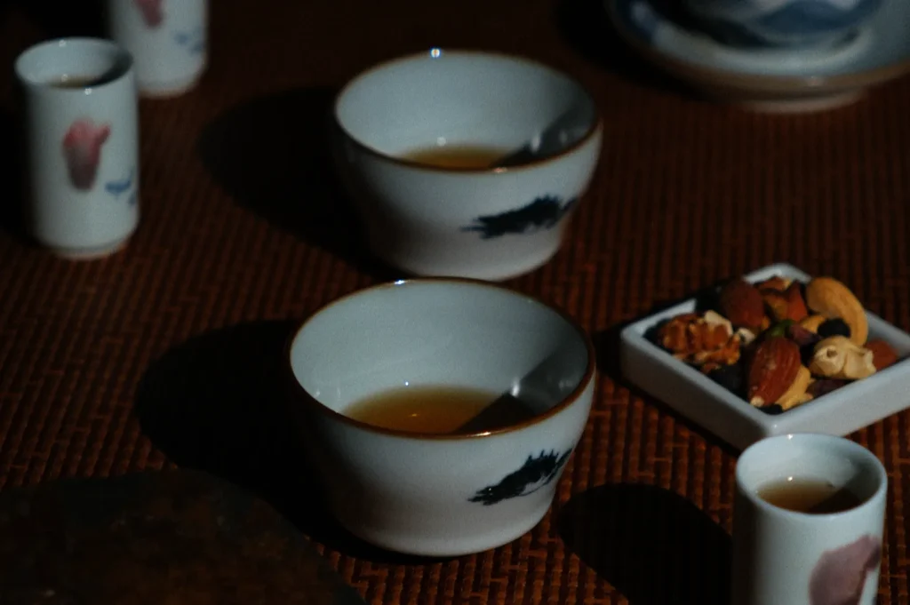 Ceramic cups with tea and a patterned design on a woven mat, accompanied by a small dish of mixed nuts, creating a warm, cozy ambiance.