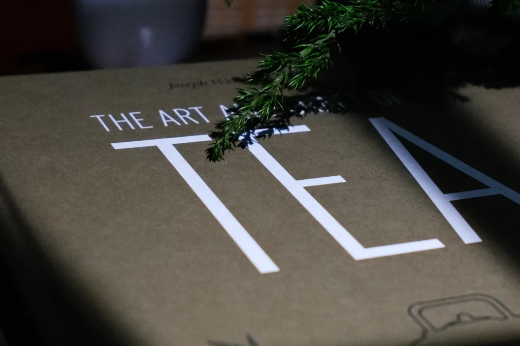 A close-up of a book titled "THE ART OF TEA," partially covered by a green branch.