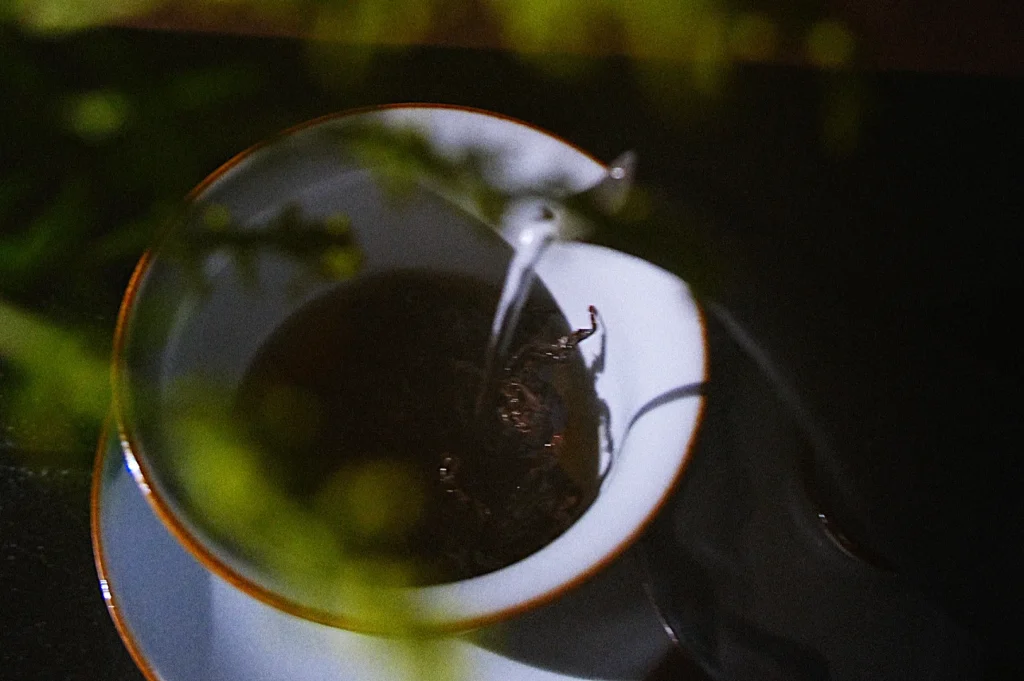 A close-up of a cup of tea being poured, with a blurred green plant in the foreground.