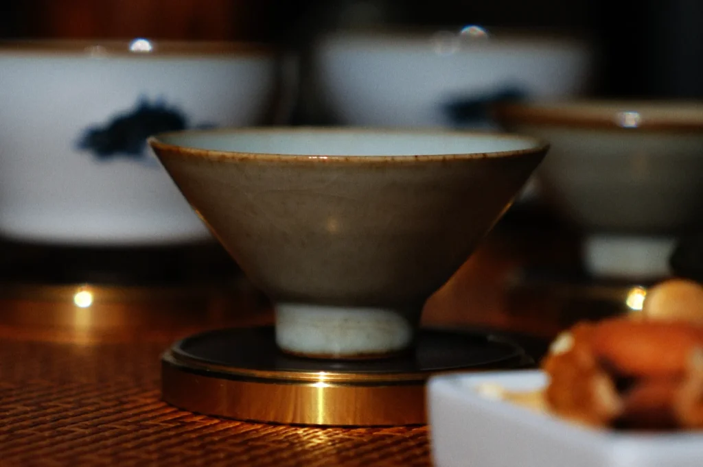 A ceramic teacup sits elegantly on a golden saucer, surrounded by blurred additional cups. The setting conveys a warm, cozy atmosphere.