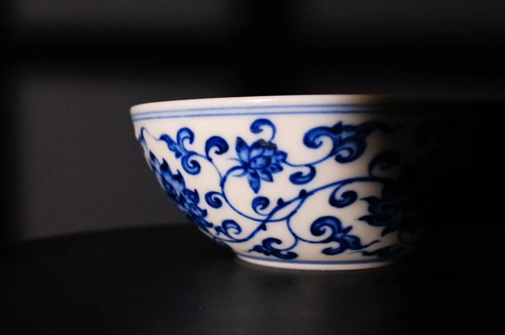 A decorative bowl with blue floral patterns on a white background, partially shadowed.
