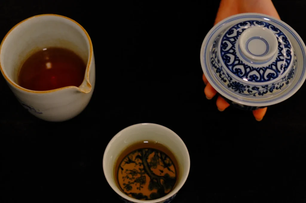 A teapot and a cup of tea with a hand holding a lid, set against a dark background.