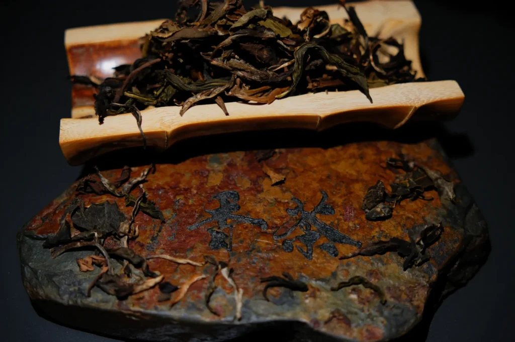 A wooden slab with dried tea leaves and Chinese characters in the middle, alongside a bamboo dish containing more dried leaves.