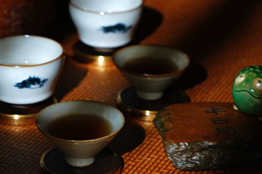 A close-up of several cups and a decorative stone on a textured surface, with light and shadow playing across the scene.