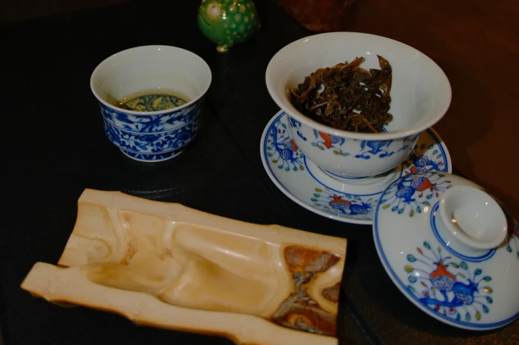 Elegant tea setup with blue-and-white porcelain cups, one filled with tea, another with wet leaves. A wooden tray adds a rustic touch. Peaceful ambiance.