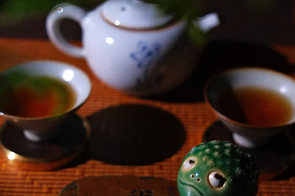 A teapot and two cups filled with tea, accompanied by a small green frog figurine.