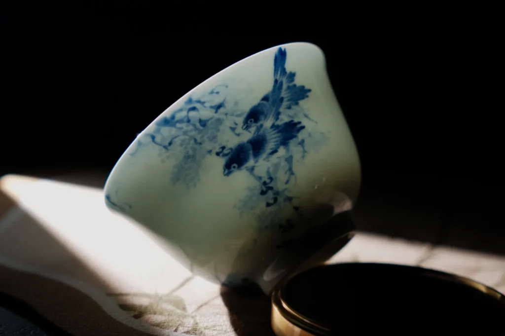 A delicate ceramic teacup with blue bird and floral designs, tilted on its side in soft light.