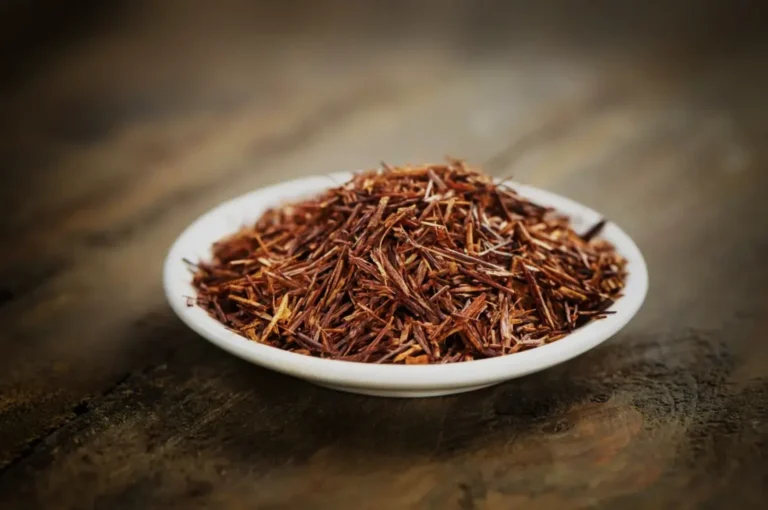 A small white bowl filled with thin, reddish-brown saffron threads resting on a wooden surface.