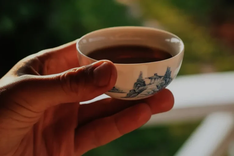 A person holding a small, decorative tea cup filled with tea.