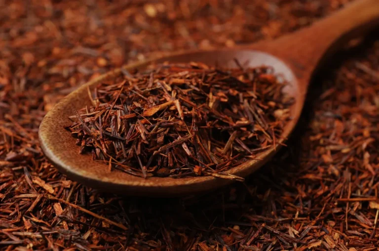 A wooden spoon filled with dried tea leaves on a background of more dried leaves.