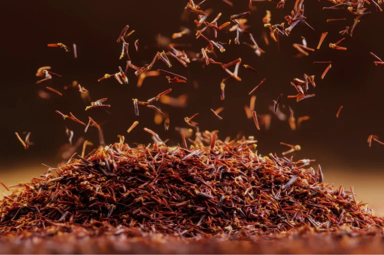 A close-up of a mound of saffron threads, with some threads appearing to float upwards against a blurred dark background.
