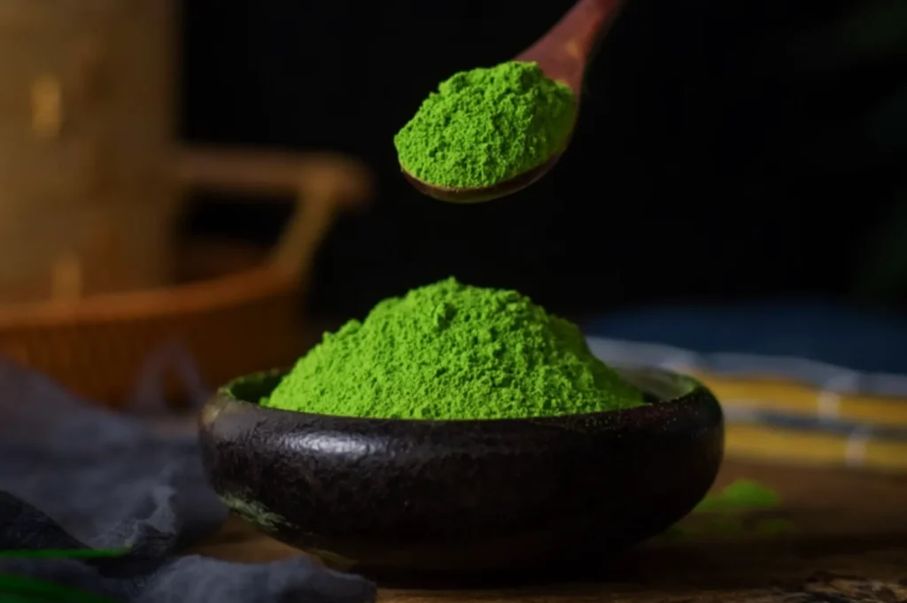 A small bowl filled with vibrant green powder, with a wooden spoon holding a scoop of the same powder above it.