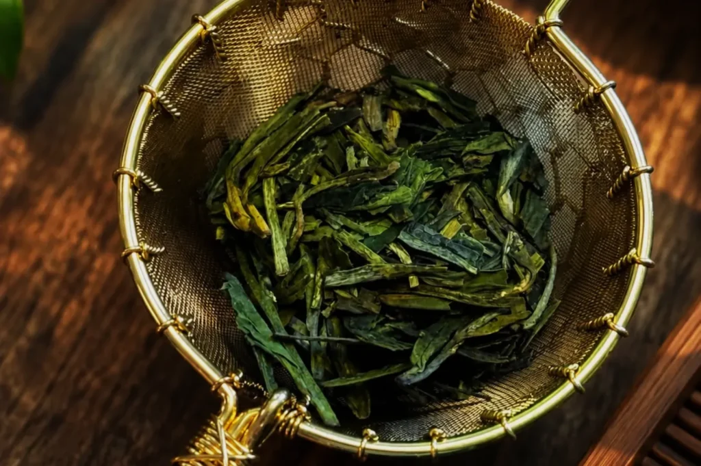 A mesh tea strainer containing loose green tea leaves.
