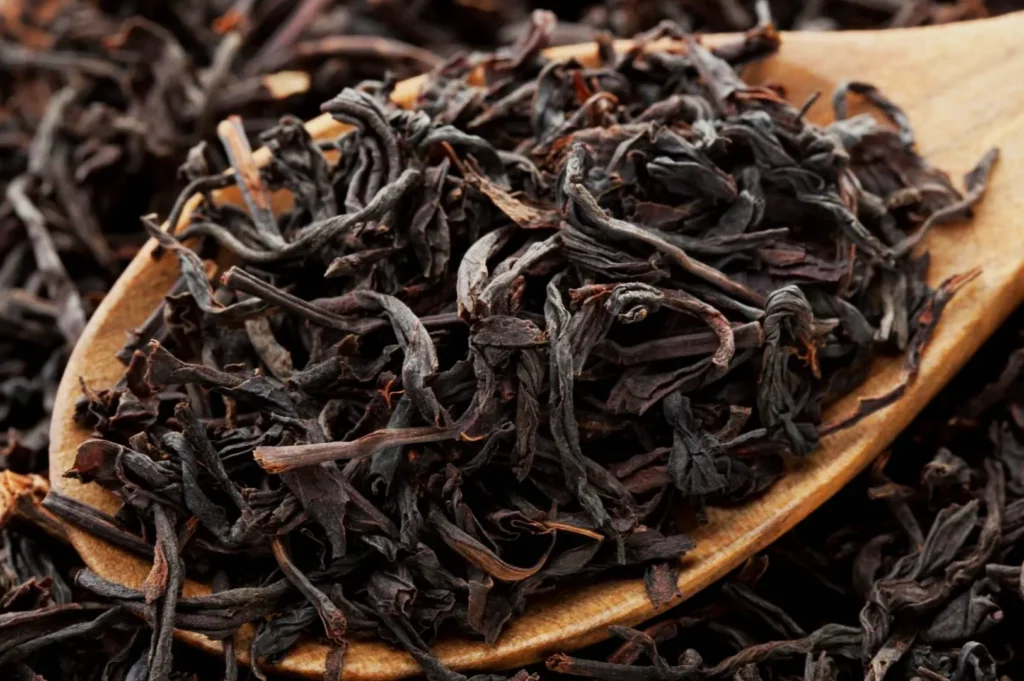 A close-up of dried black tea leaves on a wooden spoon.
