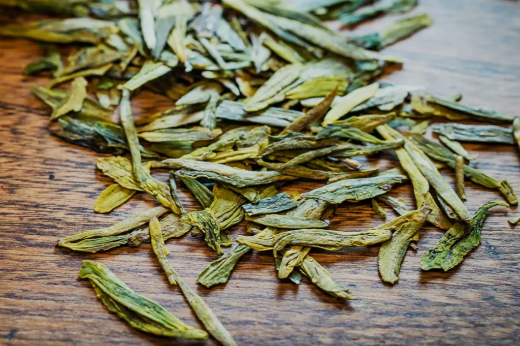 Loose green tea leaves scattered on a wooden surface.