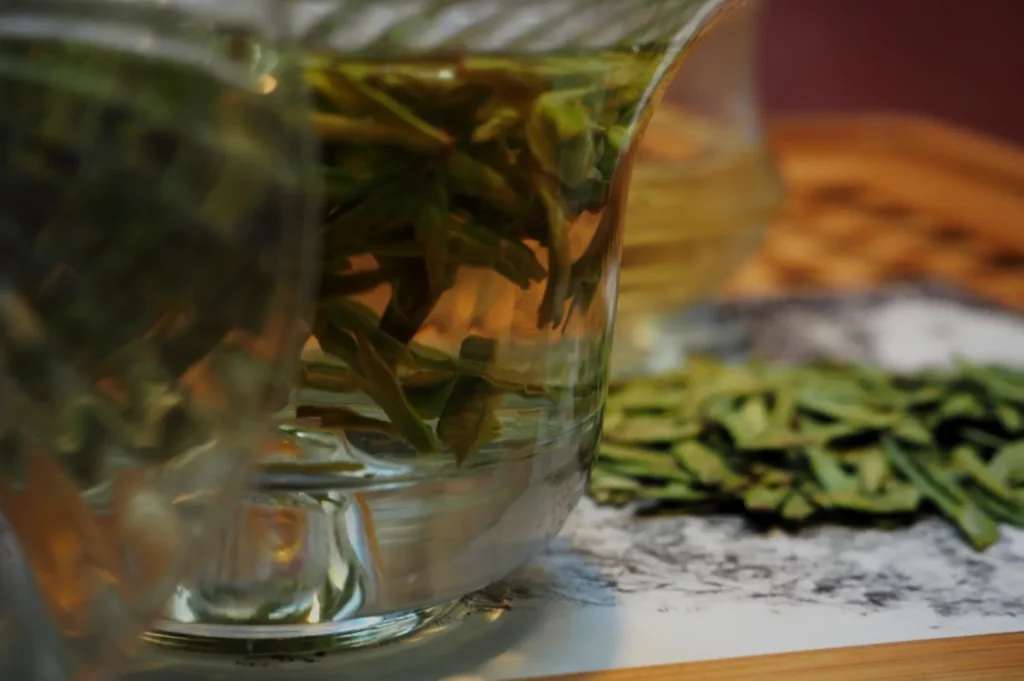 A close-up of a glass container filled with green herbs, surrounded by more herbs on a wooden surface.