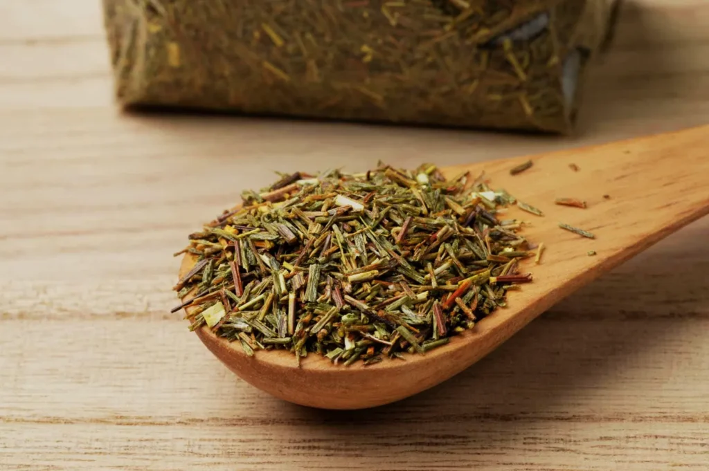 A wooden spoon filled with dried herbs on a wooden surface, with a bag of herbs in the background.