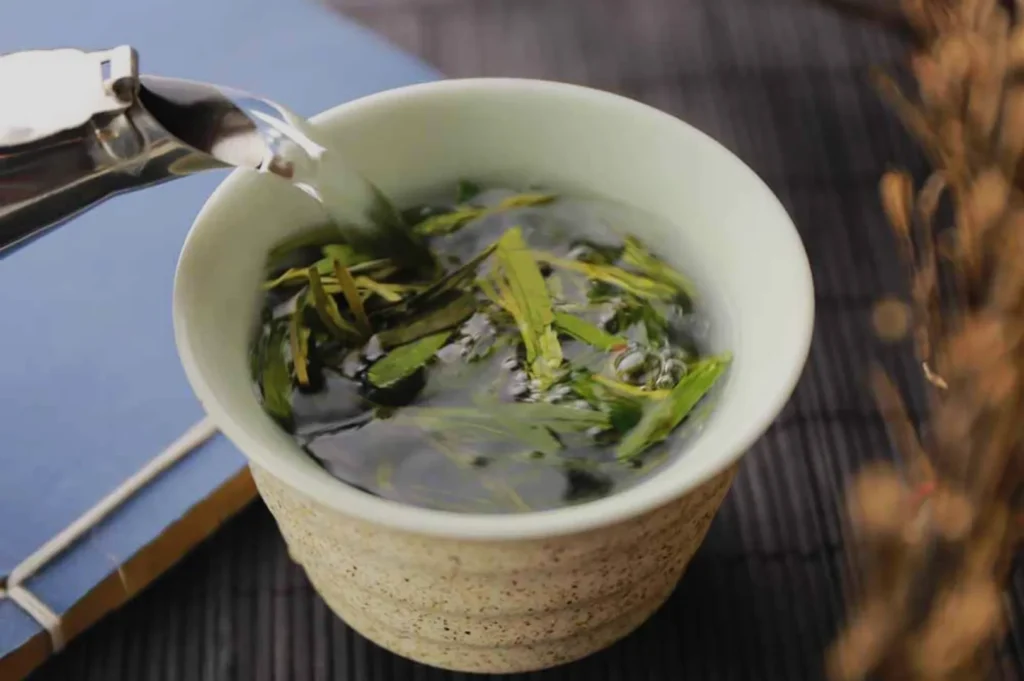 A cup of green tea with leaves steeping in hot water, placed on a surface with a textured background.