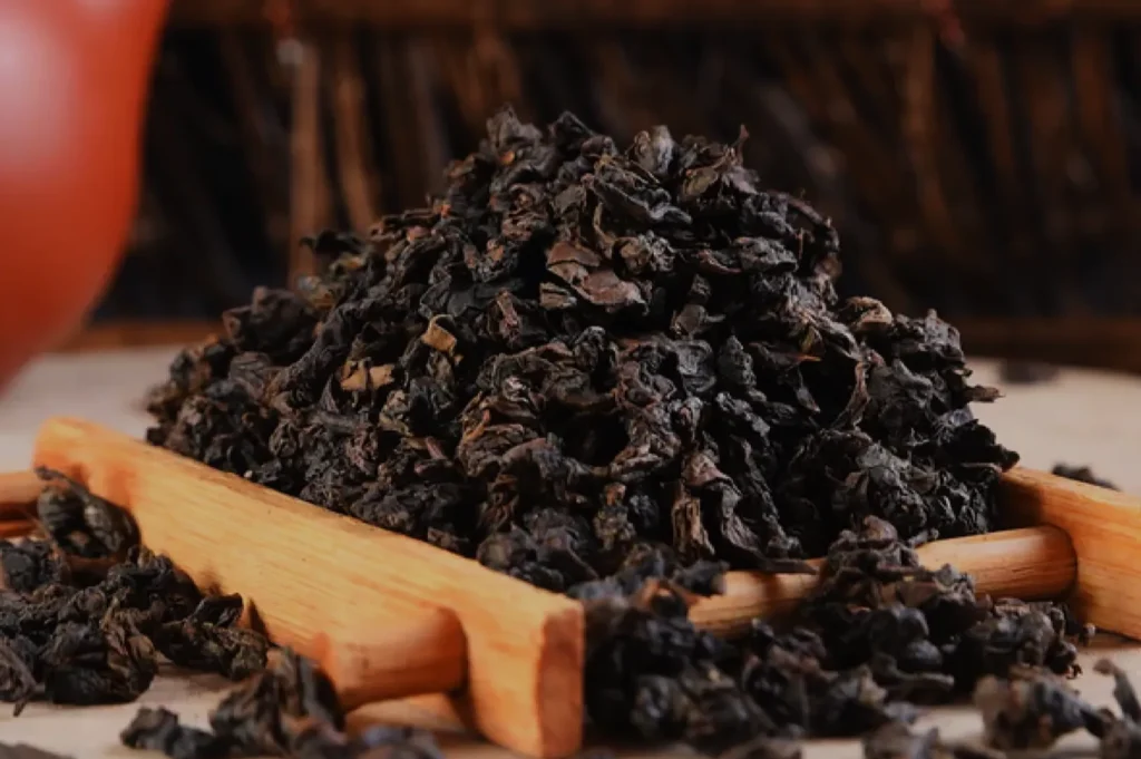 A close-up of a pile of dried tea leaves on a bamboo tray, set against a blurred background.