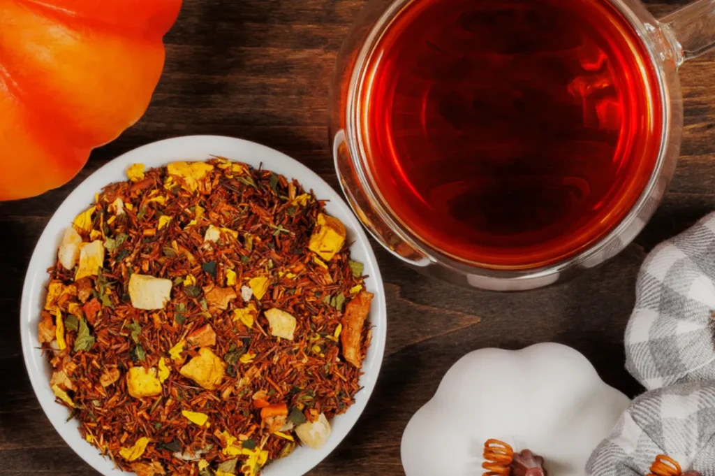 A bowl of spice mix, a cup of tea, a pumpkin, and a white decorative gourd on a wooden surface.