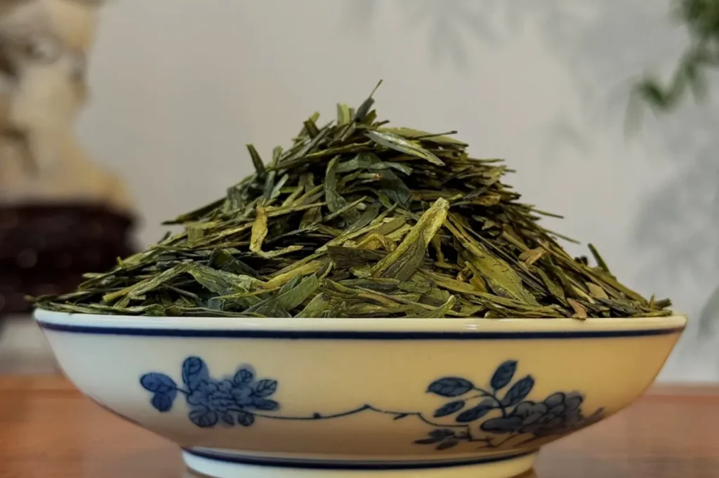 A decorative bowl filled with a large mound of green tea leaves.
