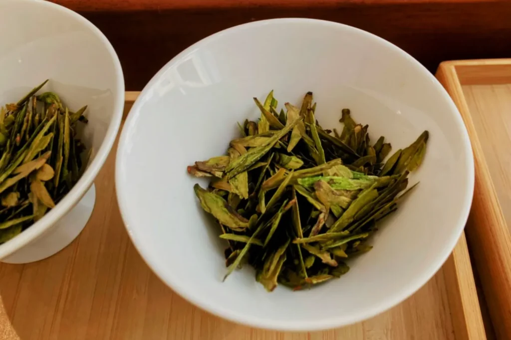 Dried green tea leaves in a white bowl.