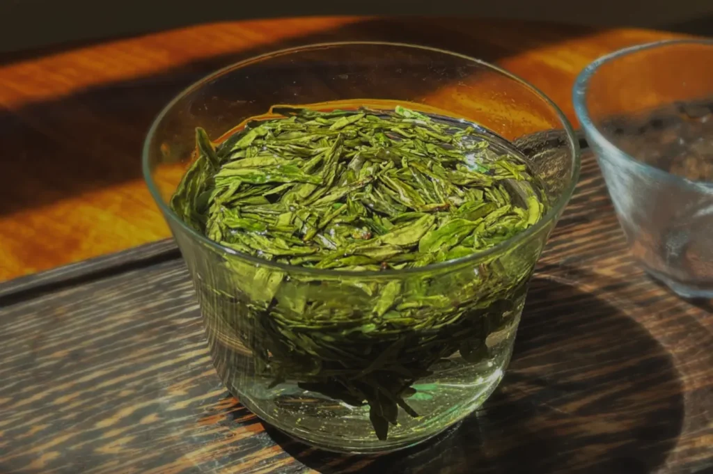 A glass containing steeped green tea leaves resting in water.