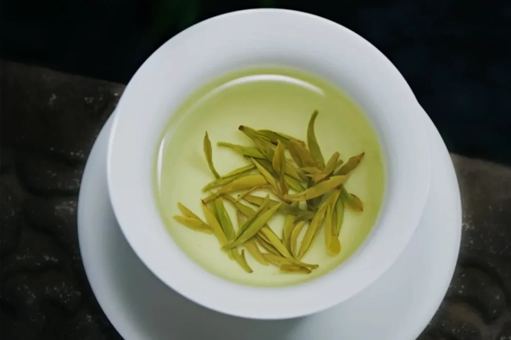 A cup of green tea with loose tea leaves floating on the surface.