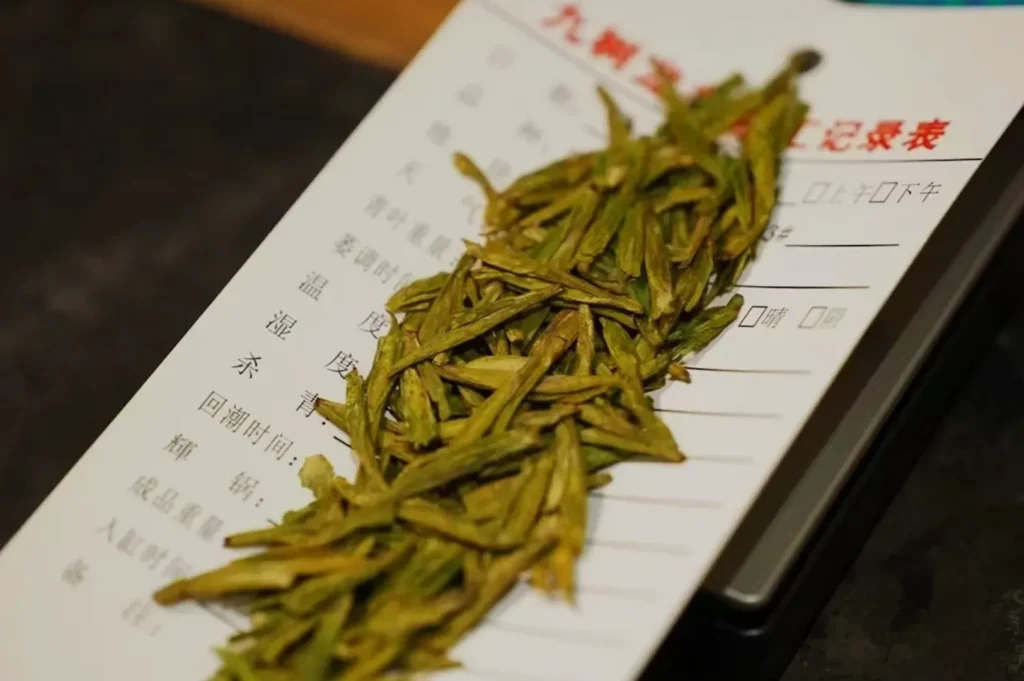 Dried green tea leaves on a weighing scale with a paper sheet underneath.