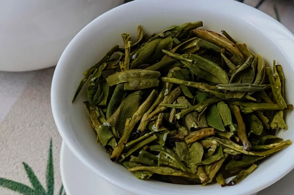 A small white bowl filled with dry green tea leaves.