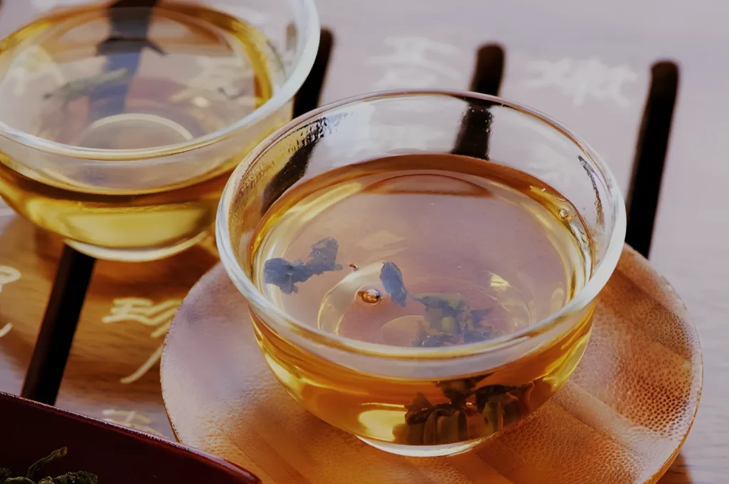 A close-up of two glass cups filled with amber-colored tea, resting on a wooden surface.