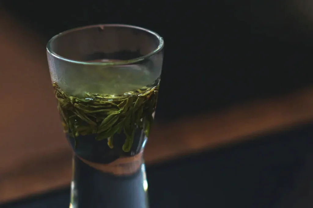 A glass shot with green tea and tea leaves submerged inside.