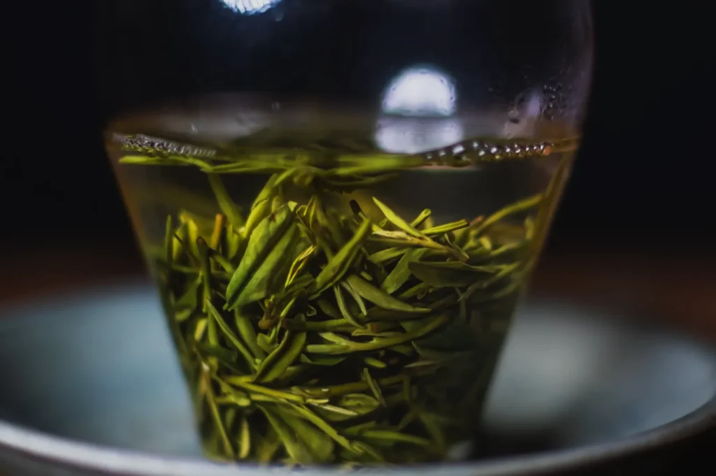 A glass container with green tea leaves steeping in water, highlighting the vibrant colors of the tea leaves against the clear liquid.