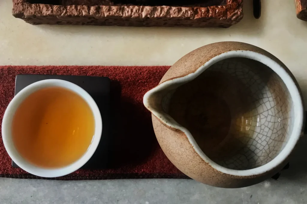 A teapot and a cup of tea placed on a textured surface, with the cup beside the teapot.